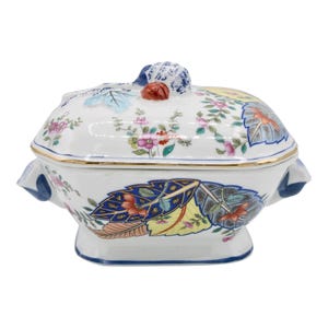 Puede incluir: Un plato de servir de porcelana blanca con tapa. El plato está decorado con un patrón floral en tonos de azul, rosa, amarillo y verde. La tapa tiene un pomo en forma de flor.