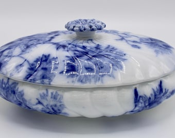 Op de afbeelding: Een witte porseleinen serveerschaal met een blauw en wit bloemenpatroon. De schaal heeft een deksel met een knop bovenop. De schaal is ovaalvormig en heeft twee handvatten aan de zijkanten.