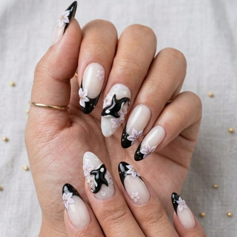 Peut inclure: Ongles en forme d'amande avec une manucure fran&ccedil;aise aux pointes noires sur une base nude transparente. Le design pr&eacute;sente des accents floraux blancs en relief et des silhouettes d'orques noires appliqu&eacute;es sur le vernis &agrave; ongles.