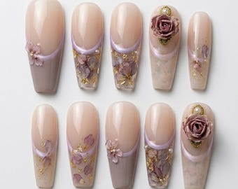 May include: A set of ten press-on nails featuring a nude base with lavender French tips, embedded dried purple flower petals, gold leaf flakes, small white pearls, and three-dimensional dusty rose floral embellishments on select nails.