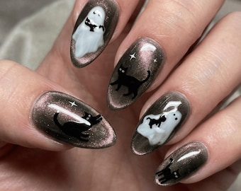Könnte beinhalten: Lackierte Fingernägel mit Halloween-Motiv. Die Nägel haben eine dunkle, schimmernde Farbe und zeigen Designs von schwarzen Katzen, weißen Geistern und Sternen. Die Nagelkunst ist detailliert und festlich.
