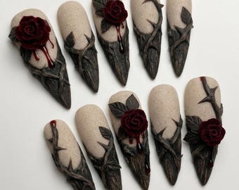 May include: A set of ten press-on nails featuring a textured beige base with dark brown, thorny vine accents. Several nails are adorned with three-dimensional deep red roses and glossy red drips, while others display intricate, sculpted brown branches.