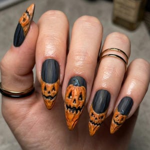 May include: Long almond-shaped nails featuring a matte black base color with three-dimensional orange pumpkin faces sculpted onto the tips. Each pumpkin design includes carved eyes, noses, and jagged mouths, creating a textured Halloween-themed manicure.