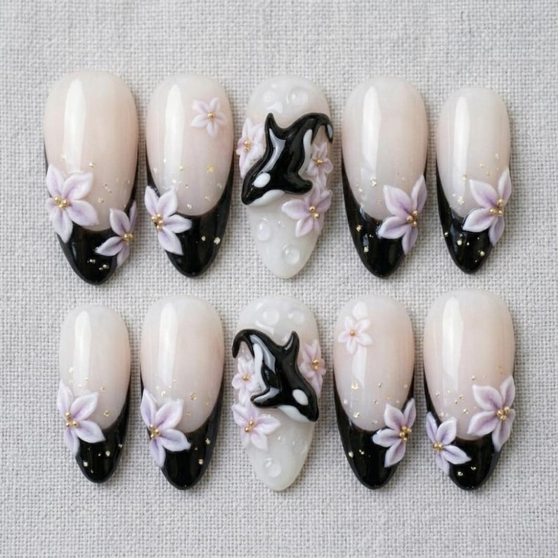 Peut inclure: Un ensemble de dix faux ongles avec une base blanc laiteux et des pointes noires. Le design comprend des fleurs tridimensionnelles violet clair avec des centres dor&eacute;s et deux ongles orn&eacute;s d'une figurine d'orque en relief noir et blanc.