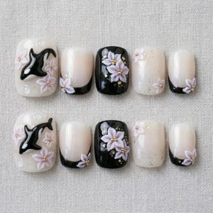 Peut inclure: Un ensemble de dix faux ongles &agrave; la finition brillante. Les motifs incluent des orques noires et blanches, des fleurs 3D violet clair avec des centres dor&eacute;s, ainsi que des pointes noires ou blanc translucide avec des paillettes dor&eacute;es.