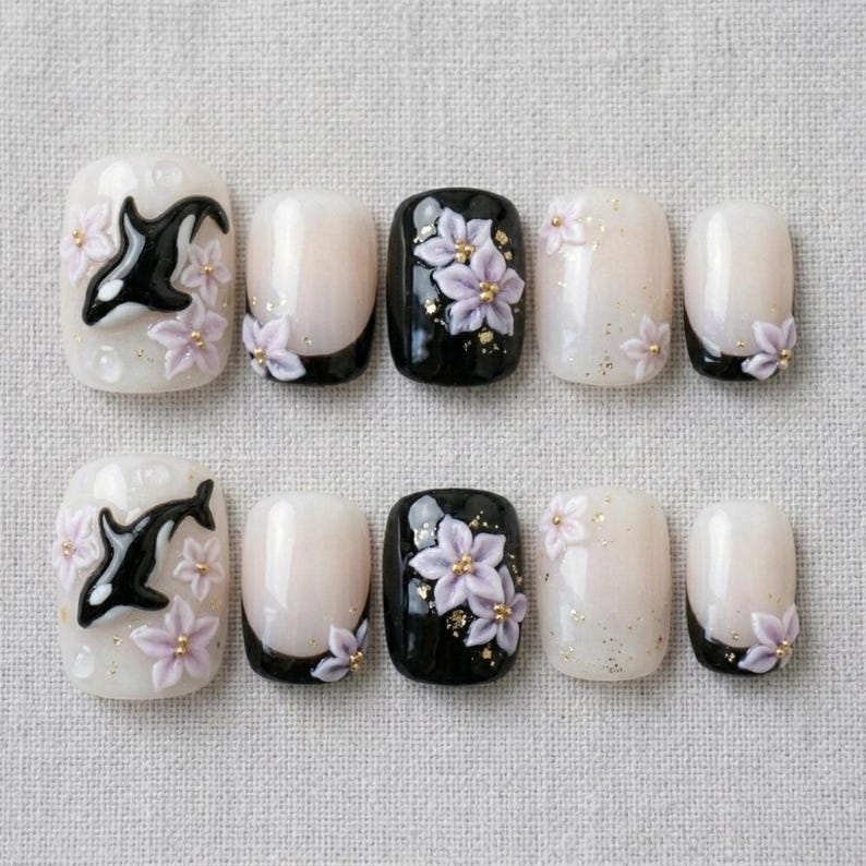 Peut inclure: Un ensemble de dix faux ongles &agrave; la finition brillante. Les motifs incluent des orques noires et blanches, des fleurs 3D violet clair avec des centres dor&eacute;s, ainsi que des pointes noires ou blanc translucide avec des paillettes dor&eacute;es.