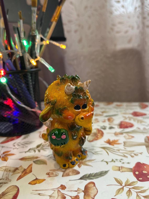 A hand-sculpted polymer clay dragon clutching a tiny magnetic frog — intricate, whimsical, and clearly made by someone with serious skill and a sense of humor.