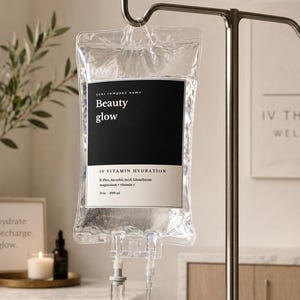 Può includere: Una sacca endovenosa trasparente con l'etichetta "Beauty glow" e il testo "IV Vitamin Hydration". La sacca è appesa a un supporto metallico. La sacca contiene un liquido trasparente. Un cartello recita "hydrate. recharge. glow."