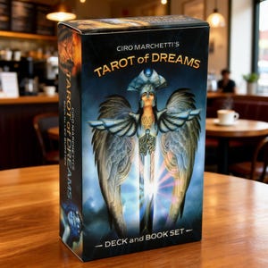 May include: A rectangular box set titled Ciro Marchetti's Tarot of Dreams, featuring a deck and book. The front displays a central winged figure in blue armor with a sword, set against a dark blue background with gold text and white accents.