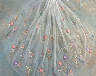 May include: A white tulle veil with delicate floral embroidery in shades of pink, purple, and blue. The veil is attached to a silver comb and features the text "Luce Veil".