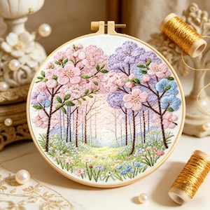 Op de afbeelding: Een gedetailleerd borduurwerk in een houten ring met een boslandschap. De bomen zijn geborduurd met roze, paarse en blauwe bloesems, met een pad dat in de verte leidt. Gouden garenklosjes liggen ernaast.