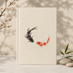 Puede incluir: Un diario de tapa dura con una cubierta de color crema texturizada que presenta una ilustración central de dos peces koi, uno negro y otro naranja, nadando en movimiento circular dentro de ondas de agua azul claro pintadas con tinta.