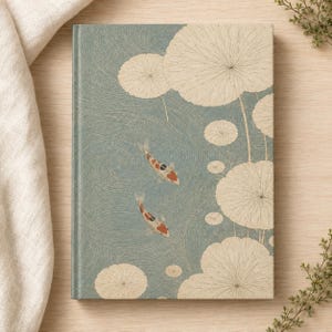 May include: A hardcover journal featuring a blue background with a swirling water pattern, two orange and white koi fish swimming, and several large, cream-colored circular lily pads with fine line details across the front cover surface.