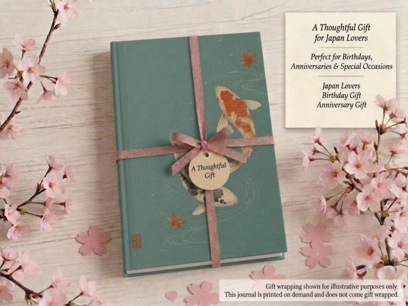 May include: A teal hardcover journal featuring an illustration of two koi fish swimming in water with scattered maple leaves. The journal is tied with a mauve ribbon and a circular tag that reads A Thoughtful Gift in the center of the cover.