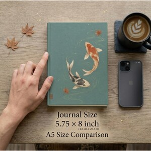 May include: A teal hardcover journal featuring an illustration of two koi fish swimming among fallen leaves. The journal measures 5.75 by 8 inches. The cover displays a graphic of a white and orange koi and a black and white koi in water.