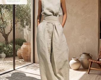 Puede incluir: Un mono sin mangas de color beige con cuello alto, una cintura ancha ajustada y pantalones sueltos de pierna ancha. La prenda está confeccionada con una tela sólida de color claro con una textura visible en todo el corpiño y los pantalones.