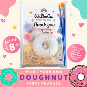 May include: A clear plastic bag containing a white doughnut-shaped item, three small paint pots in lavender, pink, and yellow, and two blue paintbrushes. The packaging features the text WilboCo. Create Play Smile Thank you for celebrating fun day!