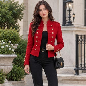 May include: A vibrant red military-style jacket featuring a high collar, long sleeves, and two vertical rows of polished gold-tone buttons. The jacket is paired with a black top, black trousers with a black belt, and a small black handbag with a gold chain.