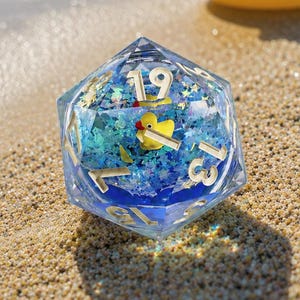 May include: A twenty-sided die with a clear resin shell containing blue liquid, glitter, and a miniature yellow rubber duck. The die features gold-colored numbers and sits on a sandy surface near a yellow rubber duck toy.