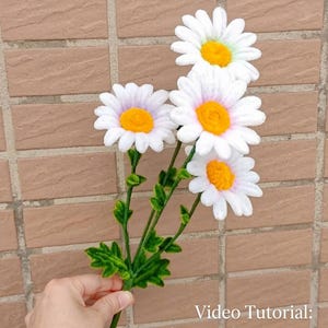 Puede incluir: Un ramo de cuatro margaritas artificiales hechas con limpiapipas blancos y amarillos, con tallos y hojas verdes. El texto en la imagen dice: Video Tutorial: Making a Shasta Daisy with Pipe Cleaners.