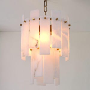May include: A modern chandelier with a brass chain and accents. The fixture features rectangular, translucent white panels with subtle veining, arranged in a tiered design. The light source is visible through the panels.