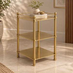 May include: A three-tier square side table with a metallic gold finish. The table features four vertical cylindrical posts with spherical finials at the top corners and a thin metal railing around the top shelf. It has three flat square shelves.