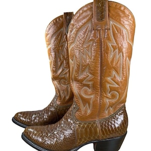 Puede incluir: Un par de botas de vaquero marrones con pie de piel de serpiente y parte superior de cuero. Las botas tienen costuras decorativas y una puntera en punta. Los tacones son negros.