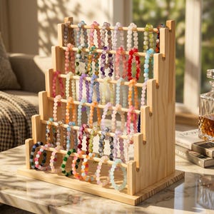May include: A tiered wooden display stand featuring five horizontal rods holding numerous multi-colored beaded bracelets. The natural light-colored wood structure has a stepped design, showcasing various translucent and opaque gemstone-style beads.