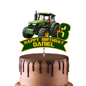 Könnte beinhalten: Ein Tortenstecker mit einem grünen und gelben Traktor, einer großen Zahl 3 und einem grünen Banner mit gelbem Text, der HAPPY BIRTHDAY DANIEL lautet. Der Stecker ist an einem gestreiften Stab befestigt und steckt in einem Schokoladenkuchen.