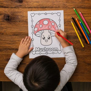 May include: A child's hands colouring a mushroom illustration with a red pencil. The mushroom has a red cap with white spots and a smiling face. The word "Mushroom" is written below the image. Colouring pencils are on the wooden table.
