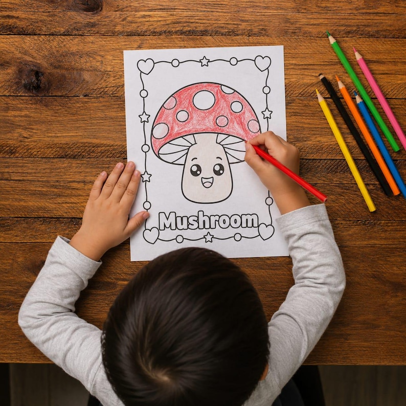 May include: A child's hands colouring a mushroom illustration with a red pencil. The mushroom has a red cap with white spots and a smiling face. The word "Mushroom" is written below the image. Colouring pencils are on the wooden table.