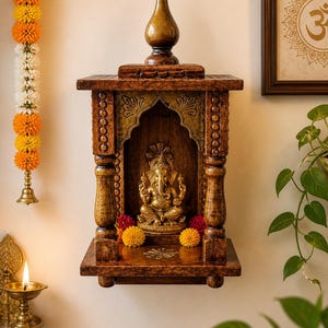 Può includere: Un santuario in legno da parete con una statua dorata di Ganesha all'interno. Il santuario marrone ha dettagli dorati ed è decorato con fiori. Un simbolo Om incorniciato è visibile nelle vicinanze.