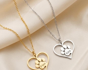Op de afbeelding: Twee kettingen met dunne schakels, een goudkleurige en een zilverkleurige. Elke ketting heeft een hartvormige hanger met een uitgesneden pootafdruk. De gouden hanger is gegraveerd met de naam Finn en de zilveren hanger met de naam Kira.