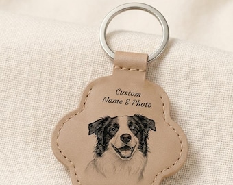 Puede incluir: Un llavero de color tostado con forma de pata y una anilla de metal plateado. La superficie está grabada con el texto "Custom Name & Photo" sobre un boceto detallado en blanco y negro de la cara de un perro con orejas caídas y expresión sonriente.