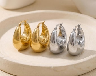 Puede incluir: Dos pares de pendientes de aro gruesos y pulidos, un par en tono dorado brillante y otro en tono plateado reflectante. Cada pendiente presenta un diseño liso, redondeado y en forma de gota con un mecanismo de cierre de bisagra.