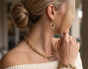 Op de afbeelding: Een goudkleurige sieradenset bestaande uit een grove schakelketting, een bijpassende schakelarmband en een paar hangende oorbellen. Elk sieraad is voorzien van een ronde hanger die is ingelegd met kleine, heldere, fonkelende steentjes.