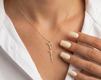 Op de afbeelding: Een goudkleurige ketting met een fijne schakelketting en een verticale hanger waarop de naam Gizem in een cursief lettertype staat. De hanger hangt centraal aan de ketting, die op het sleutelbeen van een wit overhemd rust.