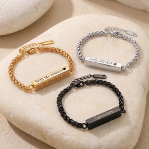 Könnte beinhalten: Drei Metallkettenarmbänder mit rechteckigen Stäben. Ein goldfarbenes Armband ist mit "With Me Always" und einem Herz graviert. Ein silberfarbenes Armband ist mit "Lucky 2002-2015" und einer Pfote graviert. Ein schwarzes Armband trägt "Your text here".