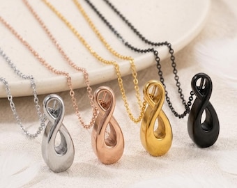 Puede incluir: Cuatro collares con colgantes en forma de infinito en tonos plata, oro rosa, oro y negro. Cada colgante presenta un diseño de bucle liso inspirado en una gota, suspendido de una delicada cadena de metal a juego, dispuestos en una fila.