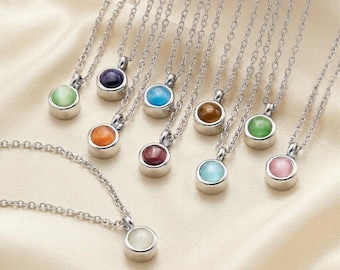 Puede incluir: Una colección de collares de tono plateado, cada uno con un pequeño colgante redondo estilo cabujón en una variedad de colores que incluyen morado, azul, naranja, verde y rosa. Los colgantes están engastados en biseles metálicos en cadenas.