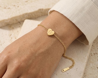 Puede incluir: Una pulsera de cadena en tono dorado con un pequeño dije en forma de corazón grabado con la letra D. La pulsera incluye una delicada cadena de eslabones y una pequeña etiqueta rectangular al final del cierre con el texto S-STEEL grabado.