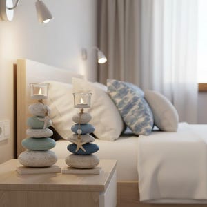 May include: Two decorative candle holders made of stacked stones in shades of blue, green, and beige. Each holder has a glass cup for a candle and a starfish accent. The candle holders are on a wooden nightstand.