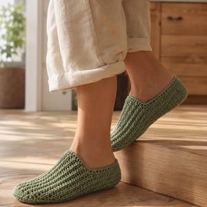 May include: A pair of sage green crochet slippers featuring a ribbed texture and a low-cut slip-on design. The slippers are crafted with a consistent knit pattern that covers the entire foot, providing a simple and functional footwear option.