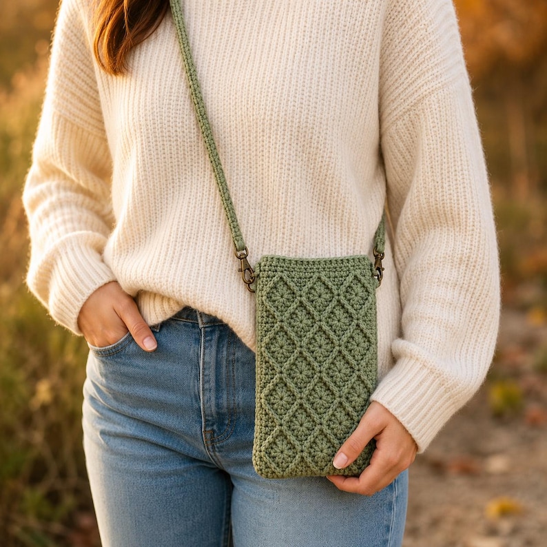 Puede incluir: Un bolso bandolera de ganchillo en color verde salvia con un patr&oacute;n de rombos texturizado en la parte frontal. El bolso incluye una correa de ganchillo a juego sujeta con cierres giratorios de metal en tono bronce para llevar objetos.