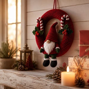 May include: A red crocheted wreath featuring a central gnome with a tall red hat, white beard, green sleeves, and black boots. The wreath is decorated with two candy canes and green holly leaves with red berries, hanging against a white wall.