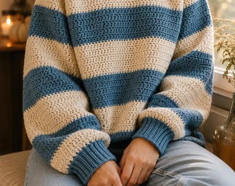 May include: A long-sleeved, crew-neck jumper featuring wide horizontal stripes in cream and blue. The garment is constructed with a visible crochet stitch pattern, including ribbed cuffs and a ribbed neckline in a solid blue colour.