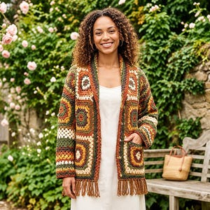 May include: A long-sleeved, open-front cardigan constructed from multi-colored crochet granny squares in shades of rust, olive green, mustard yellow, and cream. The garment features a shawl collar, two front pockets, and a fringed hemline.