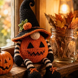 May include: A crocheted pumpkin gnome featuring a tall black pointed hat with an orange pumpkin accent, a round beige nose, and a spherical orange body with a stitched jack-o'-lantern face. It has black and white striped arms and legs with black shoes.