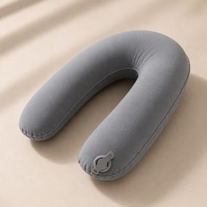 May include: A grey, inflatable travel pillow in a U-shape. The pillow has a smooth, velvety texture and a small, grey valve for inflation and deflation. The pillow is designed to provide neck support during travel.