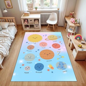 Può includere: Un tappeto rettangolare con un'illustrazione colorata del sistema solare. Il tappeto presenta pianeti sorridenti, stelle e il sole su uno sfondo sfumato azzurro e rosa. I pianeti sono etichettati con i loro nomi.